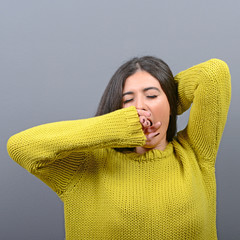 Portrait of young woman stretching and yawning against gray back