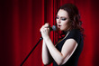 © Ulia Koltyrina - Beautiful Singing Girl on stage. Beauty Woman with Microphone. Red curtain  background