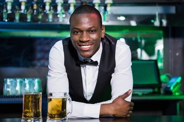 Bartender leaning on bar counter with two glasses of beer