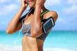 Fitness phone armband runner woman putting earphones. Closeup of sports smartphone case holder touchscreen strap on female arm of person wearing headset for running exercise cardio workout on beach.