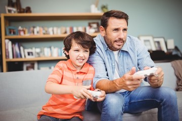 Poster - Father and son playing video game while sitting on sofa