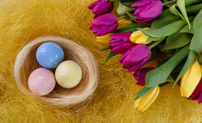 Easter painted eggs in the nest on yellow straw with spring bouquet yellow and magenta tulips.