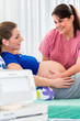 Hebamme im Kreißsaal tastet Bauch schwangerer Frau