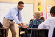© Monkey Business - Smiling teacher leaning on elementary school pupil’s desk