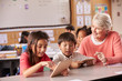Senior teacher helping elementary school pupils using tablet