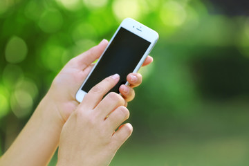 Poster - Female hands holding a mobile phone outdoors, on blurred background