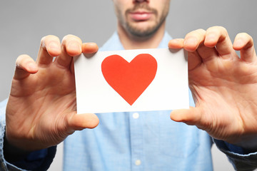 Poster - Young man holding red paper heart on grey background