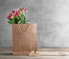 Pink Roses In Paper Bag On Wooden Table Against The Grey Wall, Close Up