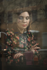 Beautiful woman sits in a cafe, holding a cup, photos behind gla