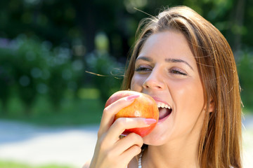 Beautiful young brunette woman bites red apple in a park