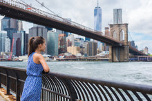New York City Urban Woman Enjoying View Of Brooklyn Bridge And NYC Skyline Living A Happy Lifestyle Walking During Summer Travel In USA. Female Asian Tourist In Her 20s.