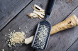 Grated horseradish root with grater on wooden gray table.