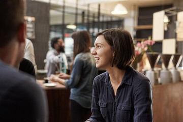 Wall Mural - Brunette woman smiling and looking away in a busy cafe