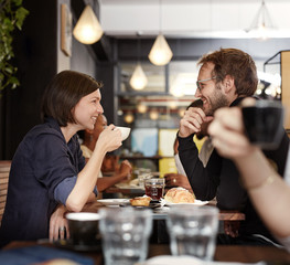 Wall Mural - Smiling couple having coffee together in a busy cafe