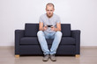 © Di Studio - young handsome man sitting on sofa with mobile phone