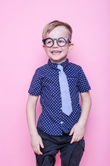 Wall Mural - Little adorable kid in tie and glasses. School. Preschool. Fashion. Studio portrait over pink background