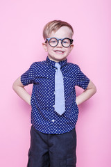 Wall Mural - Little adorable kid in tie and glasses. School. Preschool. Fashion. Studio portrait over pink background