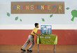 © Mint Images - A boy pushing a table into a room at the Green Science Fair,