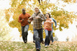 © Mint Images - A group of people, adults and young people, playing a game of football among the autumn leaves,