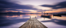Perspective View Of A Wooden Pier In The Lagoon At Sunset With Perfectly Calm Water And Reflection