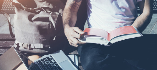 Closeup photo man wearing white tshirt sitting city park bench and reading book. Studying at the University, working new project. Books, laptop, backpack bench. Horizontal mockup