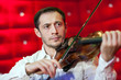 © davit85 - Young musician playing the violin in a restaurant on a red wall.