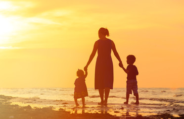 Wall Mural - mother and two kids walking on beach at sunset