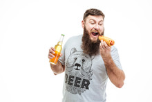 Bearded Man Holding Bottle Of Beer And Eating Hot Dog