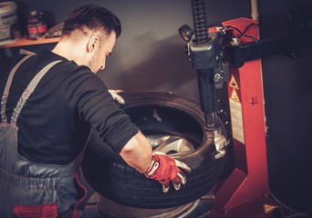 Poster - Professional car  mechanic replace tire on wheel in auto repair service.