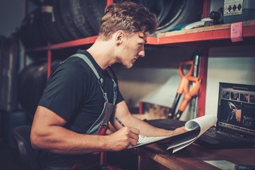 Poster - Professional car mechanic at his workplace preparing checklist in auto repair service.