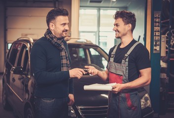 Poster - Professional car mechanic giving client keys to his repaired car in auto repair service.