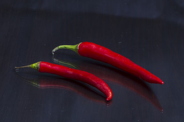 Two red  hot chili peppers are on a mirror black wooden table