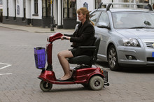 Woman Seated On A Mobility Scooter Crosses The Road At A Pedestrian Crossing