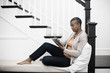 © Mint Images - Mature woman seating in hallway using digital tablet