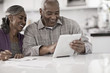 © Mint Images - A senior couple seated at a table side by side, using a digital tablet, looking at the screen,