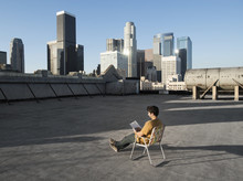 A Man Sitting In A Beach Chair On A City Rooftop Reading,