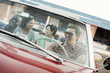 © Mint Images - A group of friends in a red convertible car on a road trip,