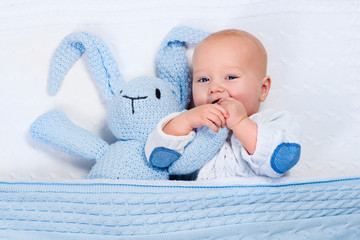 Wall Mural - Baby boy playing with blue knitted bunny toy