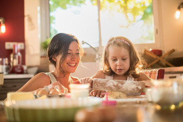 A mother and her daughter are working a pastry with a rolling pin