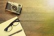 Camera, glasses and notepad on wooden background
