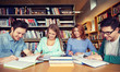 © Syda Productions - happy students writing to notebooks in library