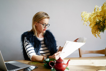 Wall Mural - Modern business woman reading a newspaper while having breakfast in the café. attractive young blonde woman put down the laptop and enjoy the morning paper and tea