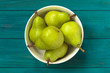 green pears in white bowl on blue wooden background, top view.