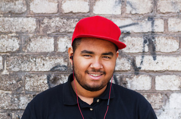 Portrait of a young black boy listening to music in headphones outdoor. Diverse and inclusive male model. Overweight POC posing by the brick wall in the city street