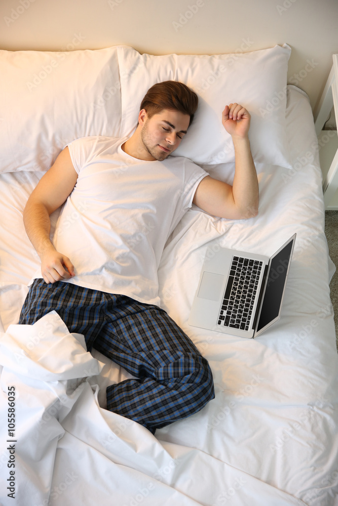Young man sleeping in bed with laptop at home