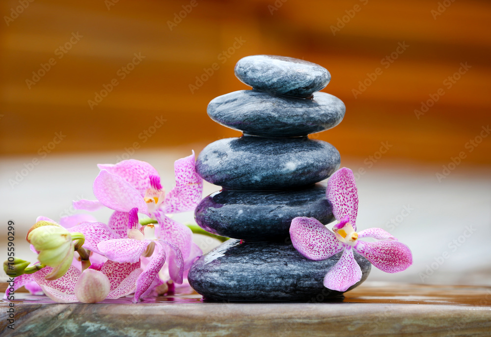 Stack of spa stones with pink orchids on wooden wet bridge