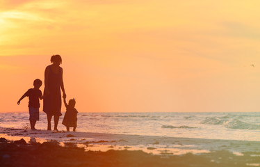 Wall Mural - mother and two kids walking at sunset beach