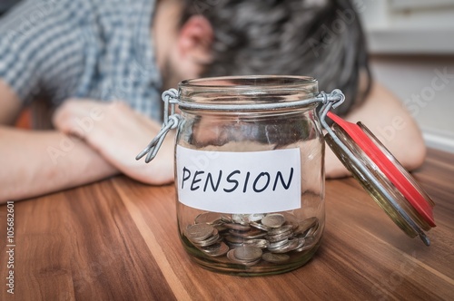 Fotografía Depressed man lying on table. Pension savings in jar in front.