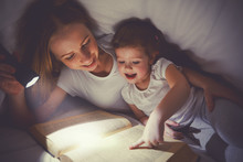 Family Reading Bedtime. Mom And Child Reading Book With A Flashl