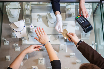 Young woman trying on golden bracelet, man paying with credit card